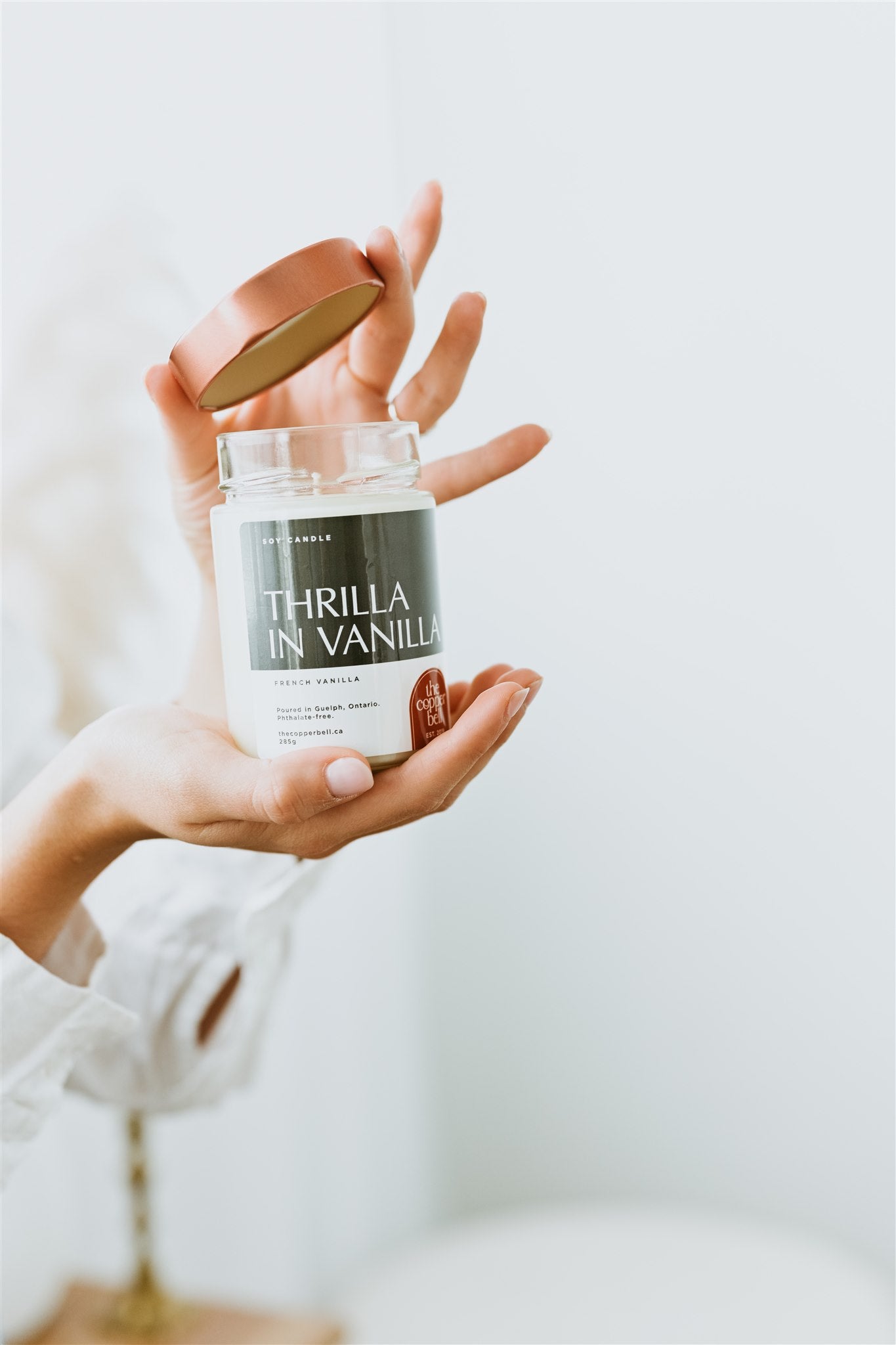 french vanilla scented candle pictured held in a woman's hands. she's lifting the copper lid off the candle slightly.