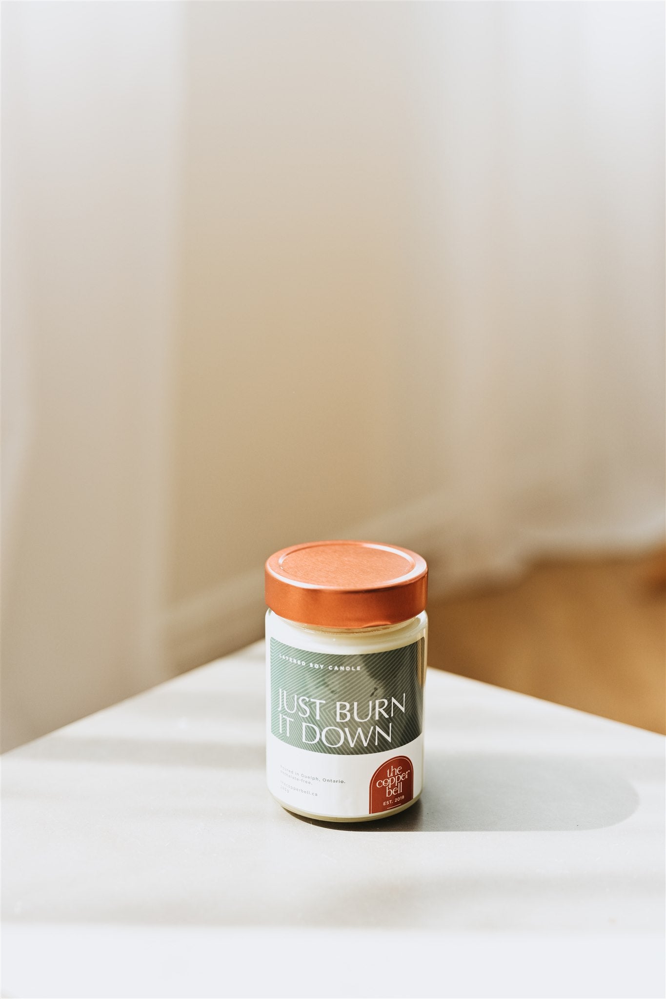 funny soy candle displayed on a white table. the lid and label are bright colours and the label reads just burn it down