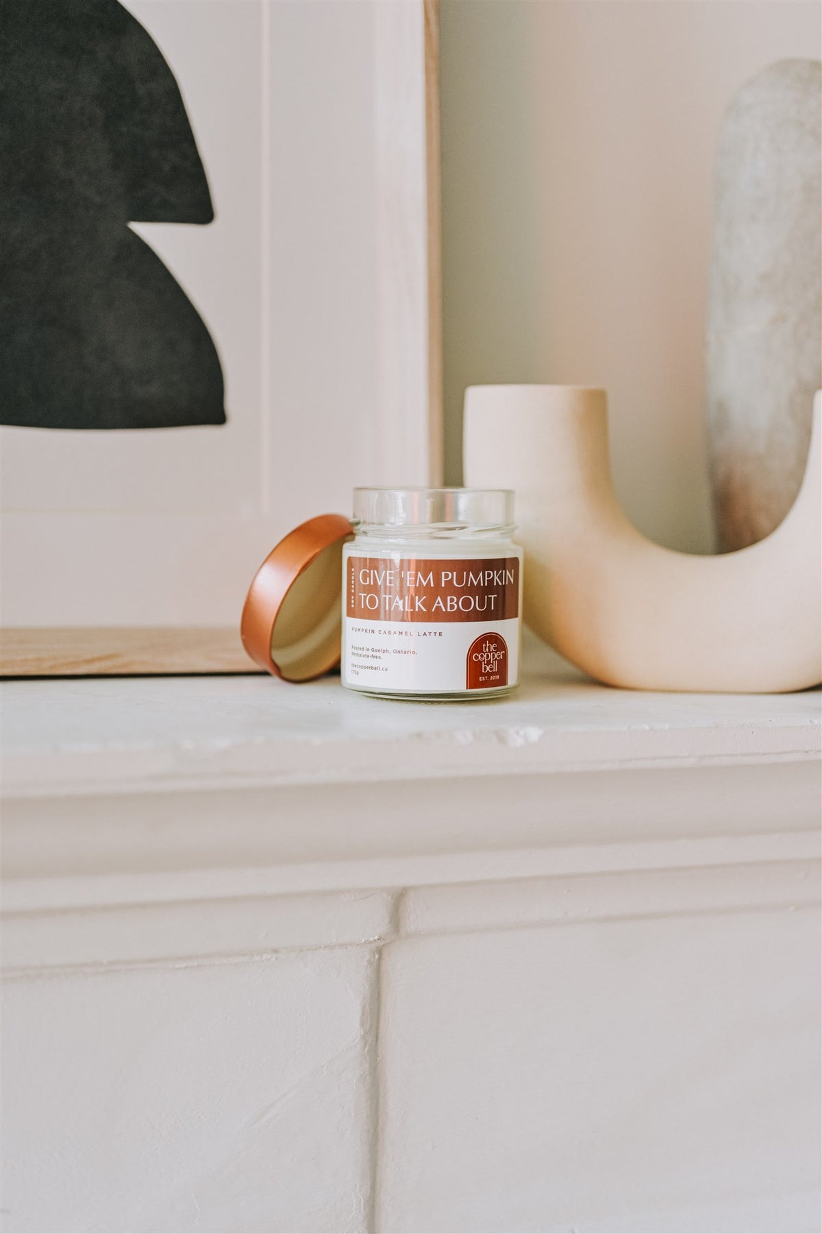 pumpkin caramel latte scented candle made by the copper bell. displayed on a white fireplace mantel.
