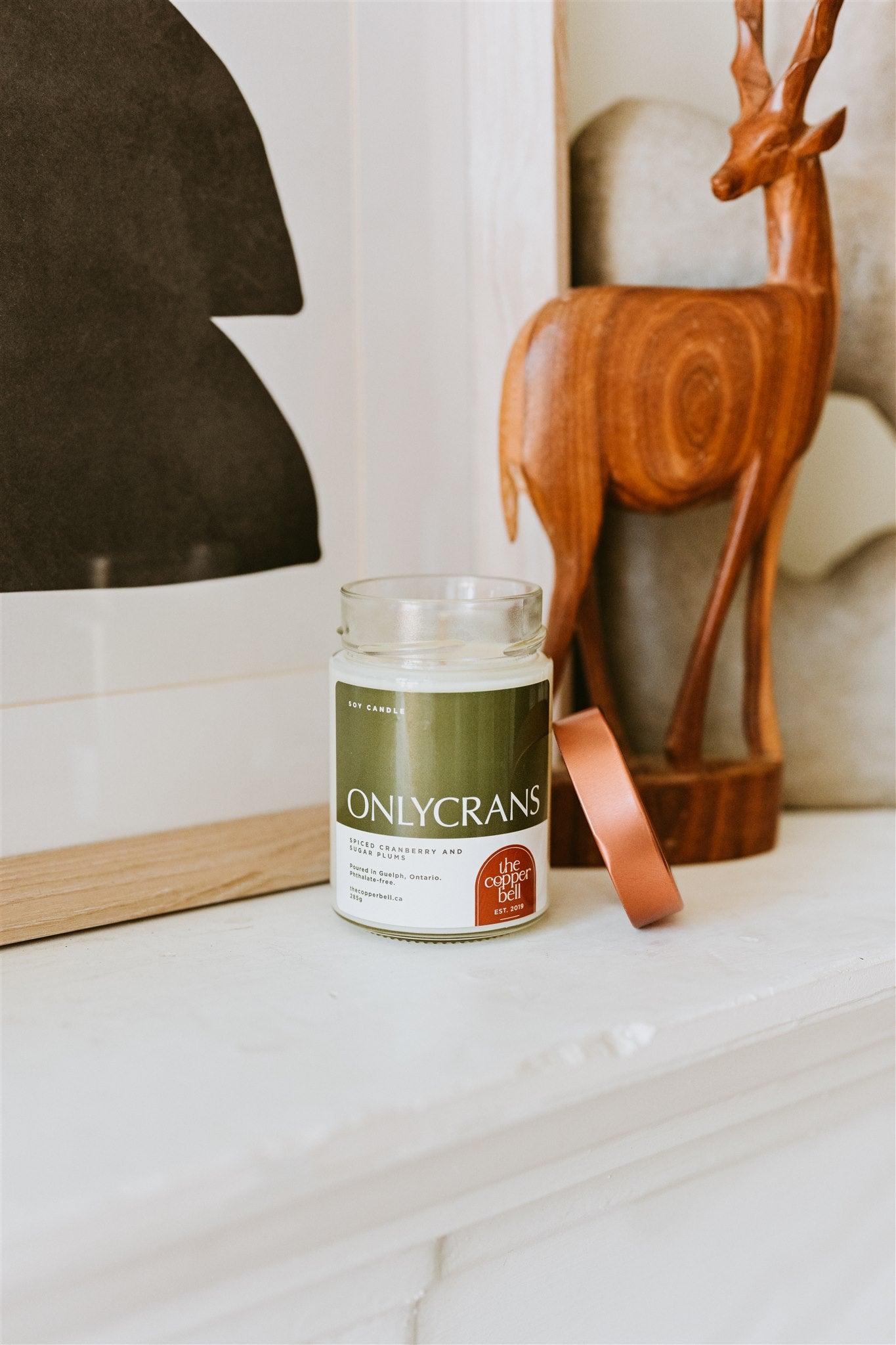 onlycrans candle displayed on a white mantel with a wooden reindeer beside it. christmas candle for cozy season.