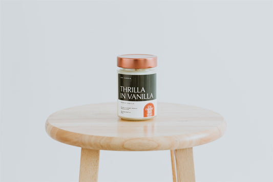 thrilla in vanilla scented candle. french vanilla scented candle pictured against a white backdrop on a wooden stool.