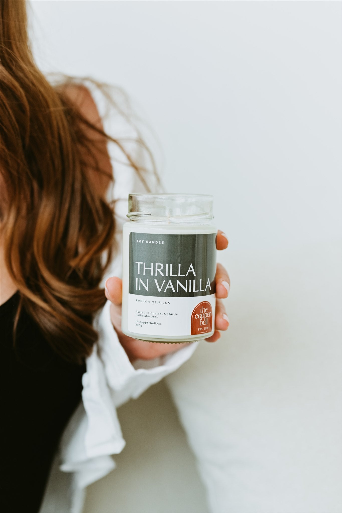 thrilla in vanilla candle held by a brunette woman wearing a black and white shirt.